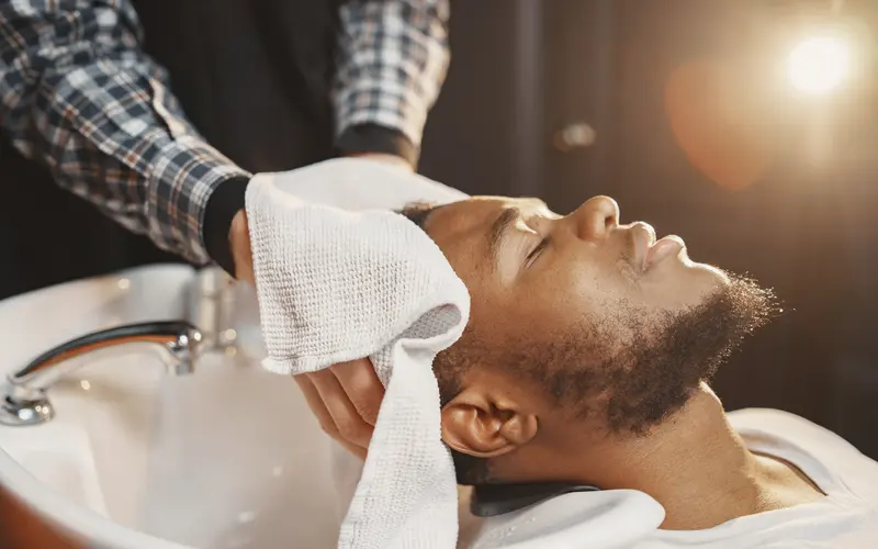 Barber wrapping a relaxed client in a clean white towel at the wash basin